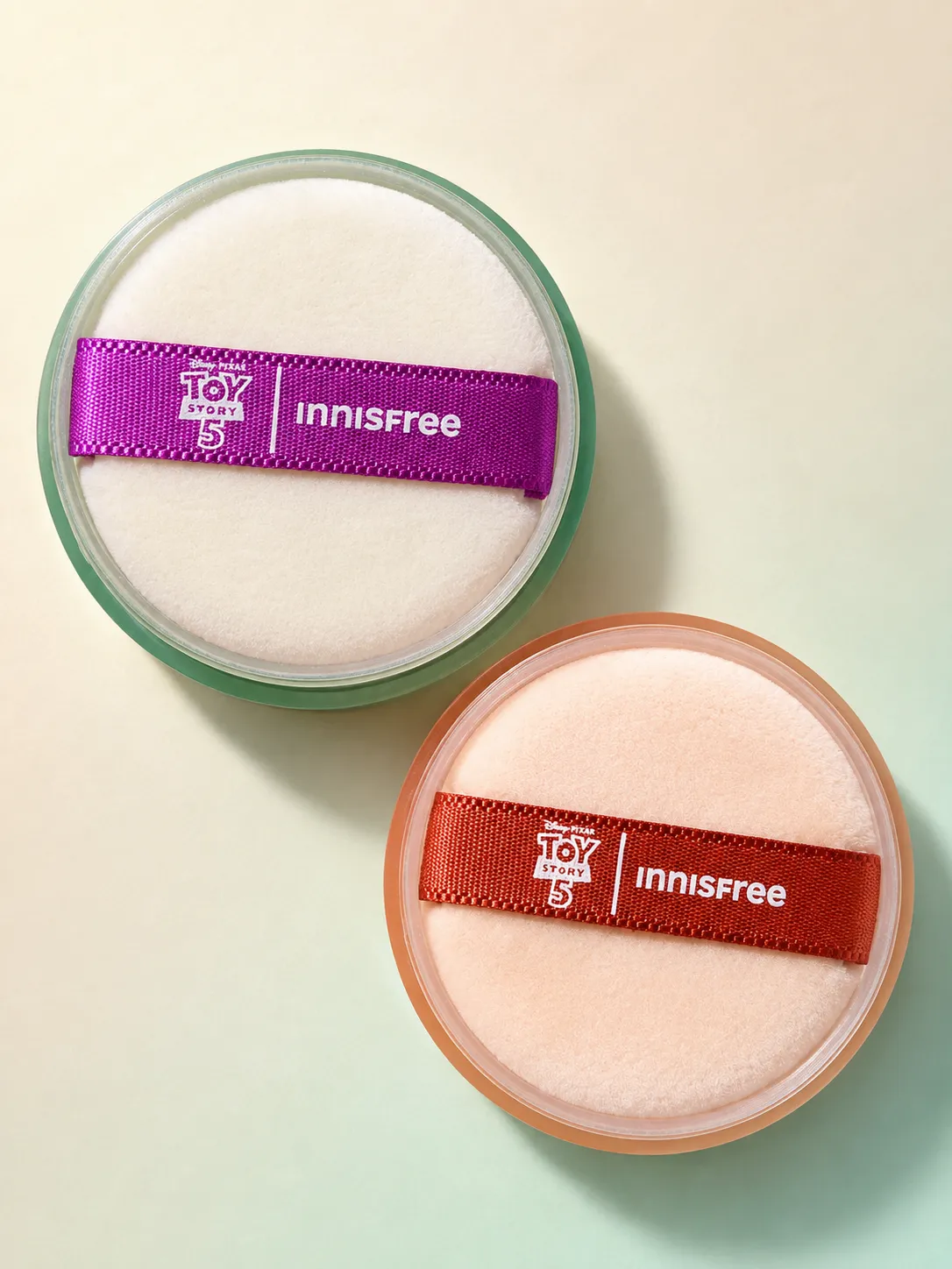 The two No-Sebum Mineral Powder jars with their Toy Story 5 x innisfree ribbon puffs, green and orange